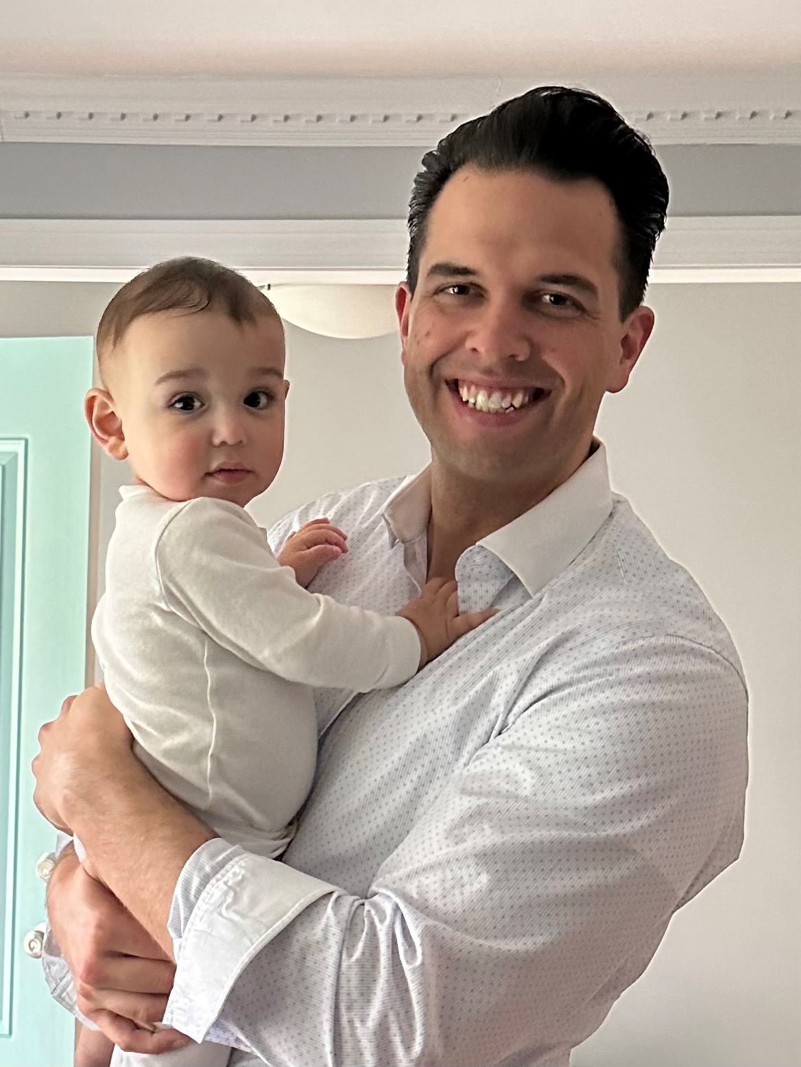 Working parent with brown hair in white shirt smiles while holding baby